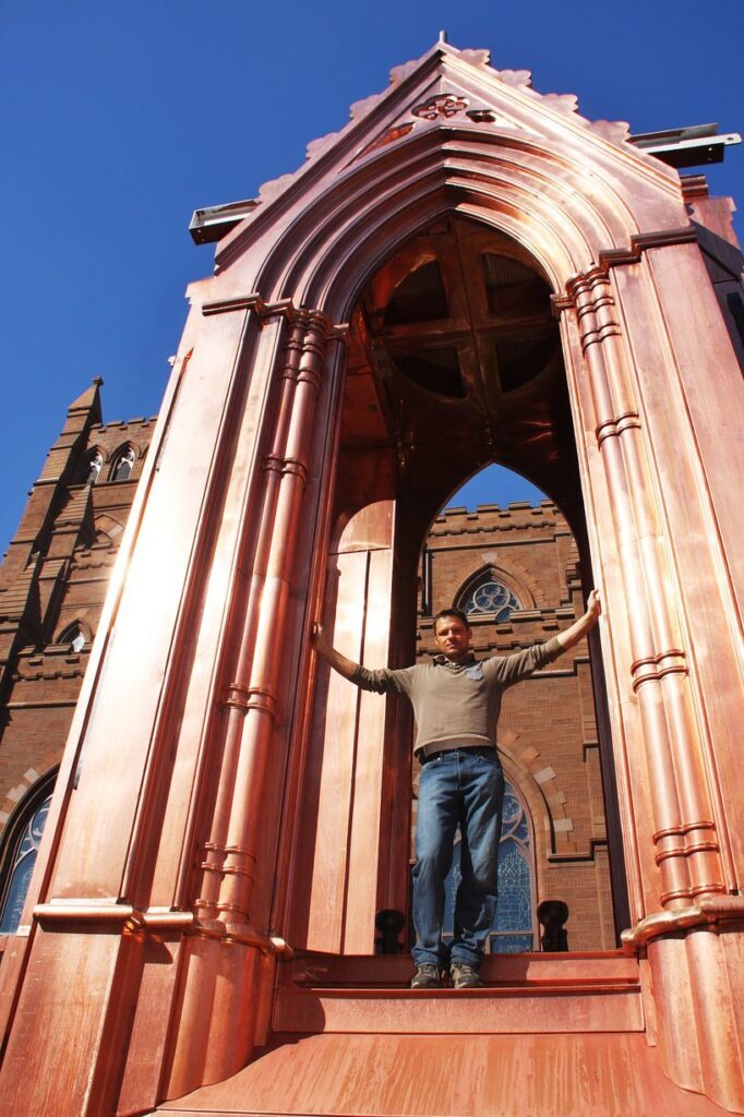 Erno standing under a copper arch built by him